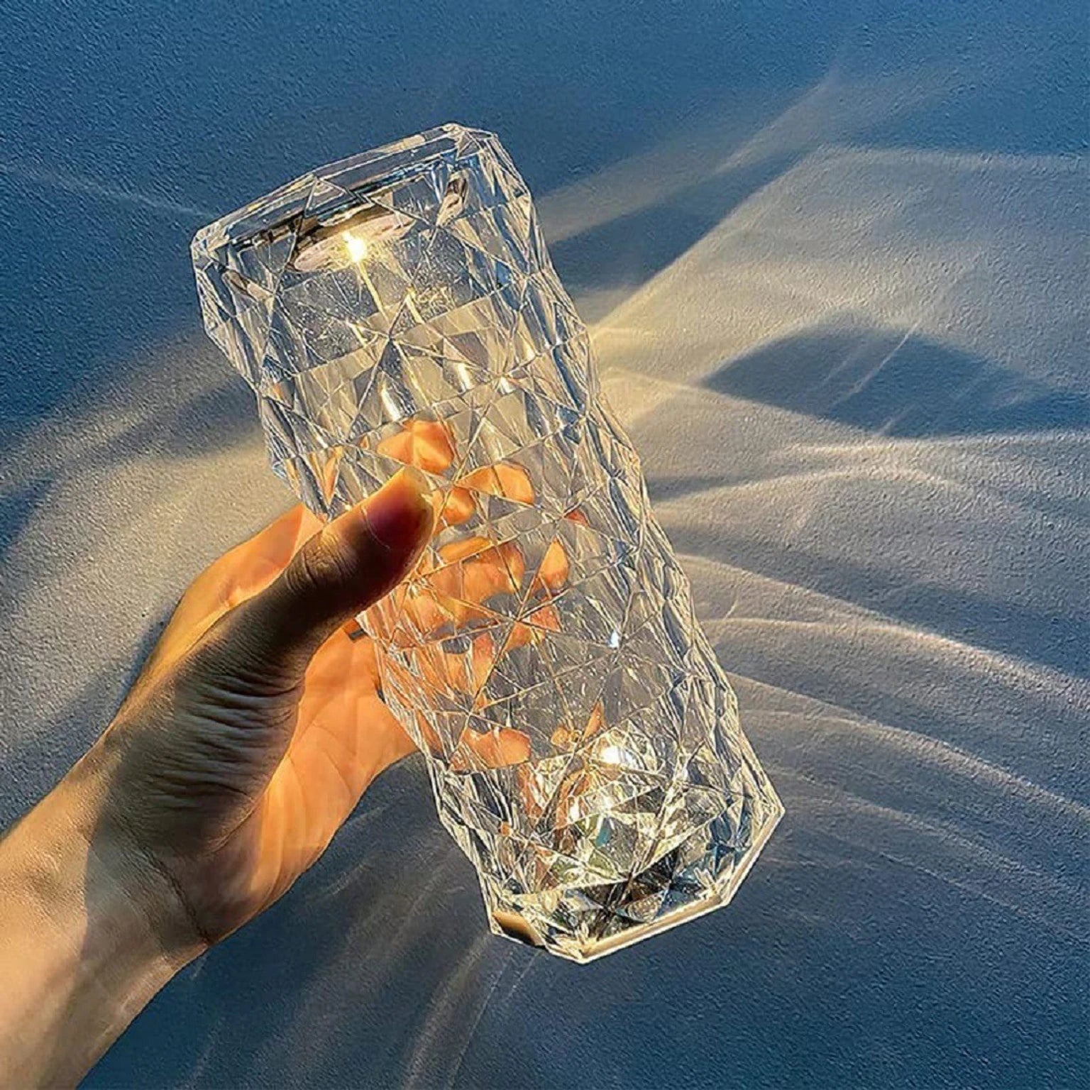 Hand holding a clear, faceted glass object against a blue sky background